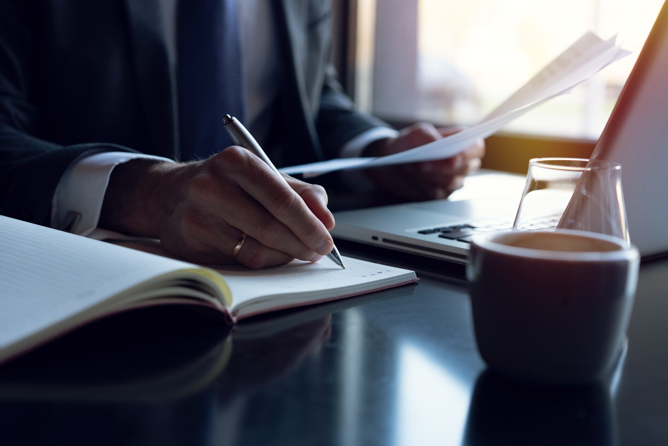 A man's hand writing an exit strategy in a notepad.