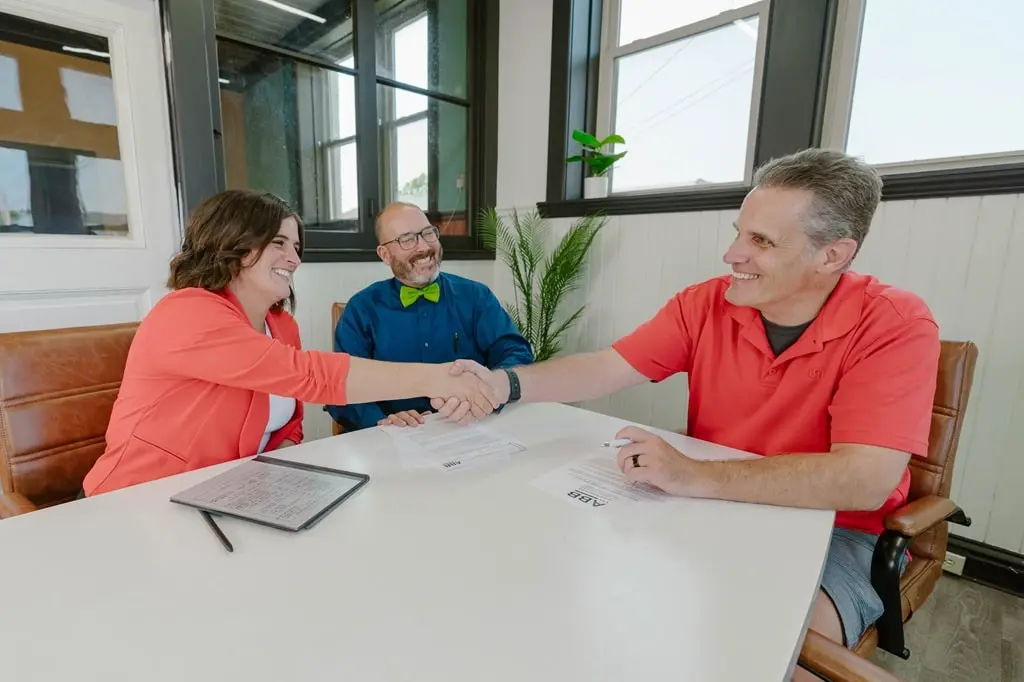 A business owner shakes hands with a buyer of their business, with a business broker assisting in the deal.