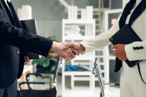 Two professional businesspeople shake hands, holding tablets in their other hand.