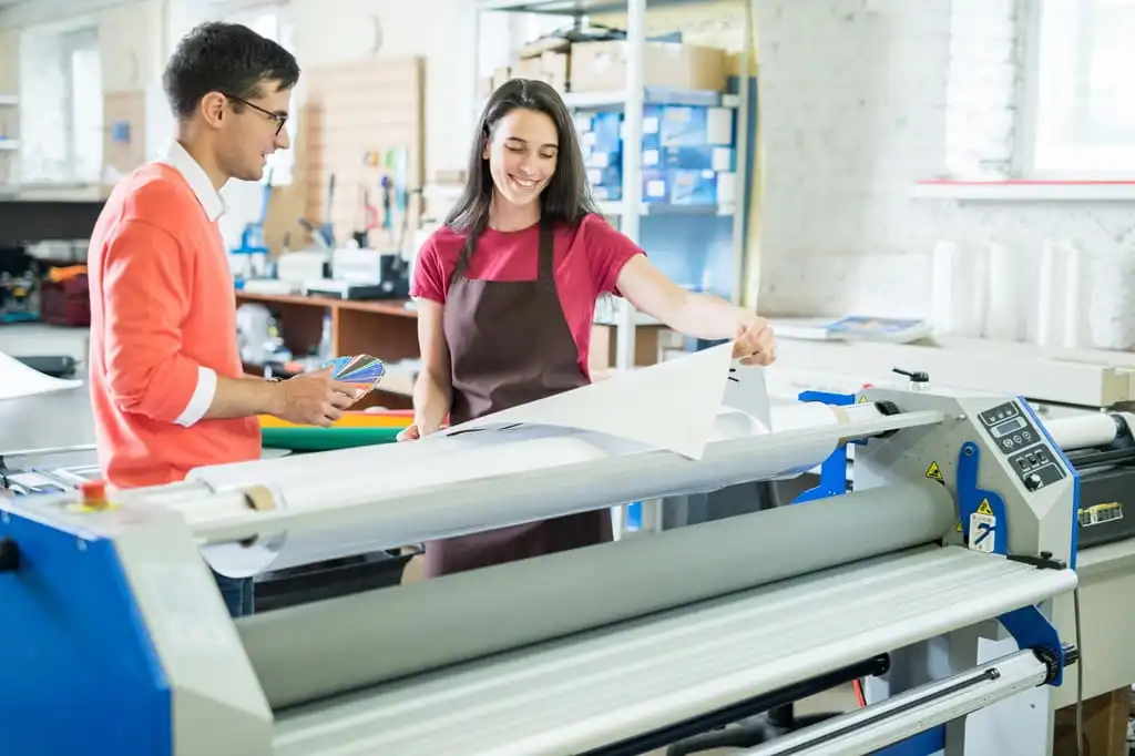 A young man a woman working in a print business, looking at large format printer paper and a color swatch.